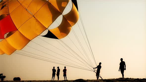 Silhouettes of people on the beach, They inflate the parachute