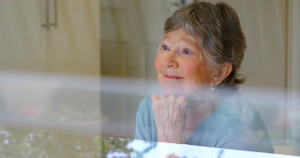 Smiling senior woman looking through the window 4k