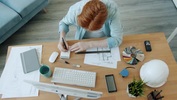 High Angle View of Specialist Architect Working with Blueprint Measuring Plan Indoors at Home