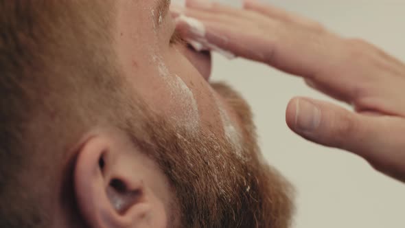 Smoothing cream on the face of a bearded guy