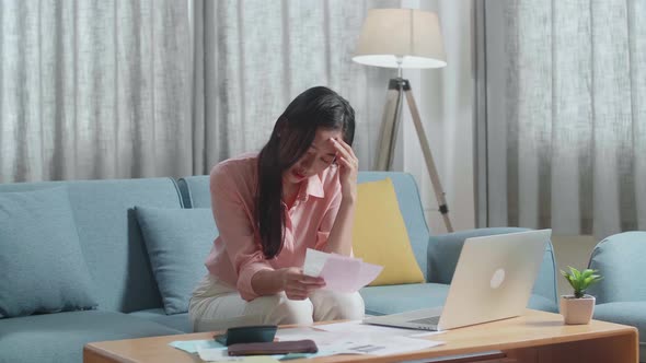 Asian Woman With A Laptop Looking At The Bill And Having A Headache Due To Financial Problem