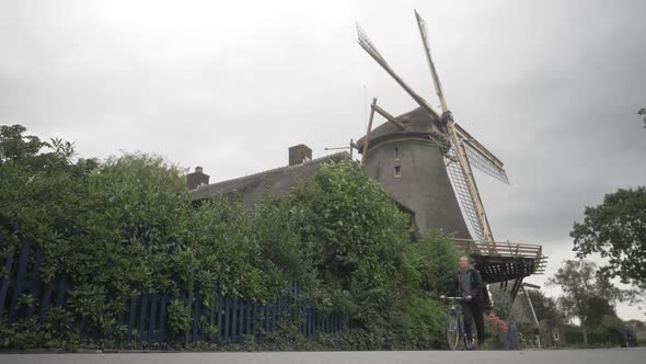 Young Dutch Woman Walking With a Bike Past a Beautiful Windmill.