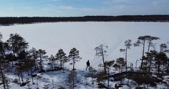 A Man is Walking Out of the Forest to the Frozen Lake