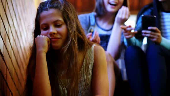 School friends bullying a sad girl in school corridor