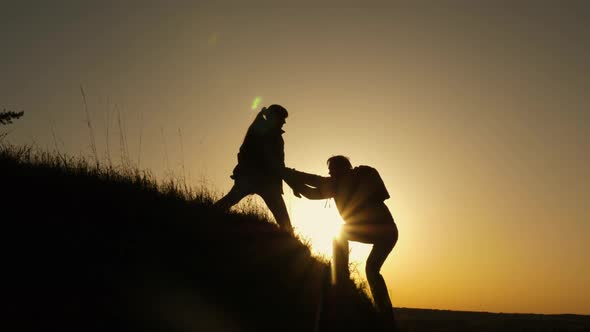 Woman Traveler Stretches a Hand To a Man Climbing To the Top of a Hill. Travelers Climb the Cliff