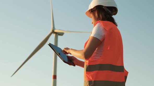 Female an Engineer in a Helmet and an Orange Vest Controls the Operation of a Wind Turbine Using a