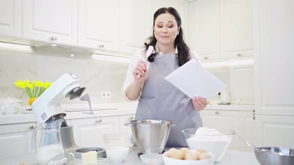 a Woman Cook with a Recipe Ingredients and a Mixer Prepares Pastries