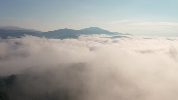 Drone flight over low clouds and morning mists covered mountain slopes