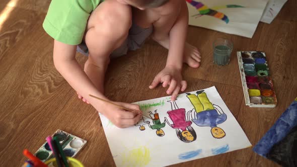 A Child Paints a Drawing on the Floor with Watercolors