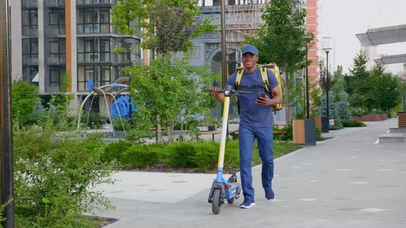 Afroamerican Man Courier Walks with Electric Scooter Uses Smartphone Navigate