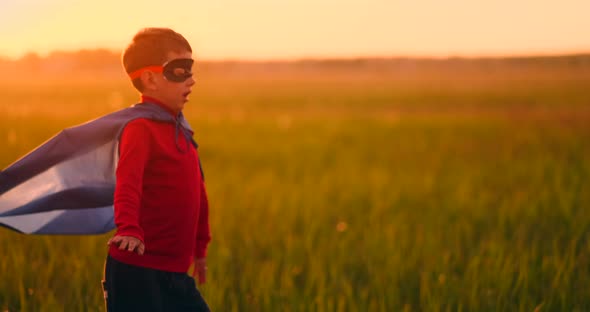 A Boy in a Superhero Costume at Sunset Runs Across the Field Laughing and Smiling