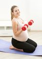 pregnant woman sitting on mat and exercising with weights - PhotoDune Item for Sale