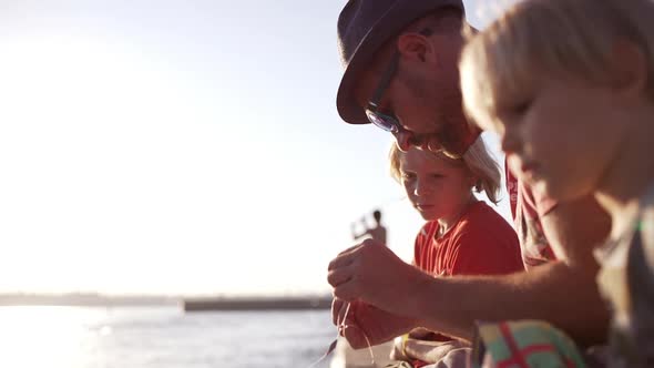 Young Caucasian Father with Light Bristle and Hat Fishing with Tow Blonde Sons in Red Shirts Sitting