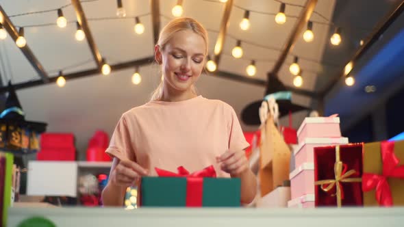 Front Lowangle View of Young Woman Seller Holding and Using Ribbon to Tie Bow for Wrapped Gift Box