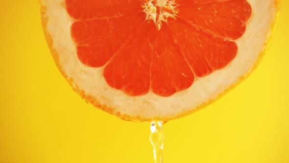 Water flows down from a slice of grapefruit on an orange background. Slow motion.