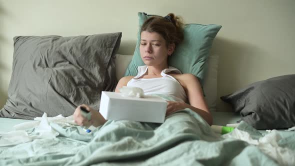 sick woman lies in bed and switches channels with the remote control from the TV