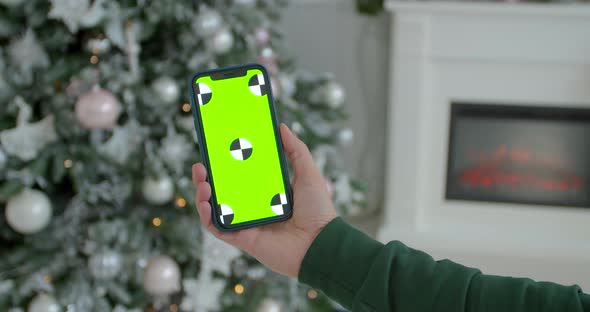 Man Holding a Mock-up Smartphone Greenscreen Chrome Key in New Year Decorated Room. Closeup of Male