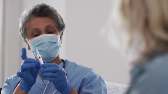 Senior african american female doctor wearing mask preparing vaccination for woman at home