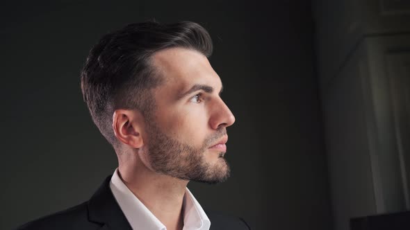 Serious Young Elegant Business Man Posing at Dark Office Near Window