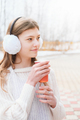 young girl drinking coffee in a park. teenager wearing earmuffs and holding coffee to go - PhotoDune Item for Sale