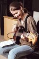 young smiling woman playing bass guitar and reading chord notes at band rehearsal. vertical size - PhotoDune Item for Sale