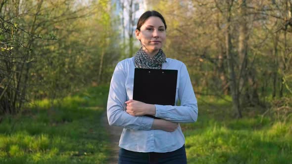 A Woman Walks Through the Park with a Folder in Her Hands