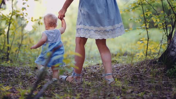 mother with a one-year-old child walks through the woods or park. first steps of the child