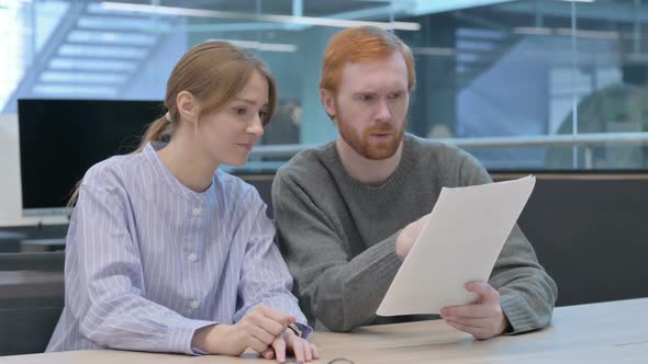 Young Man and Woman Reading Documents in Office