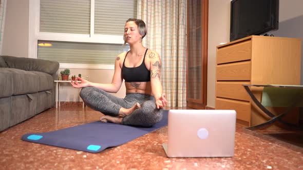 Woman performs yoga breathing and greets her online class using computer