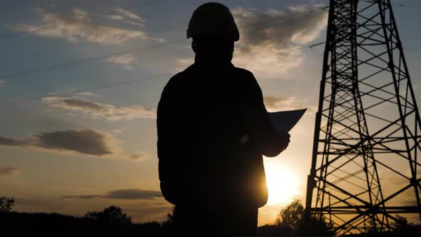 Silhouette of Engineer Standing on Field with Electricity Towers. Electrical Engineer with High