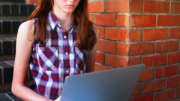 Smiling schoolgirl using laptop on staircase