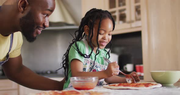 Happy african american father and daughter baking, preparing pizza in kitchen