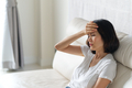 Asian woman having headache sitting on sofa. She puts one hand on her head and closing her eyes. - PhotoDune Item for Sale