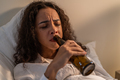 Drunk Latino woman hold beer bottle, and crying feel hangover on bed. - PhotoDune Item for Sale