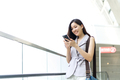 Asian office girl playing mobile phone standing on elevator in shopping mall. - PhotoDune Item for Sale
