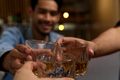 Close up of glasses clinking between group of friends drinking whiskey at night party in bar. - PhotoDune Item for Sale