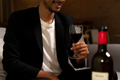 Crop shot of man sitting on sofa holding glass of wine with smile before drinking. - PhotoDune Item for Sale
