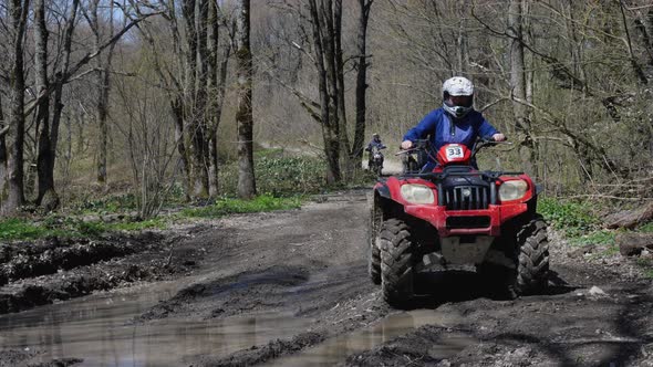 Red ATV with a girl behind the wheel riding through a puddle in the spring forest. Front view