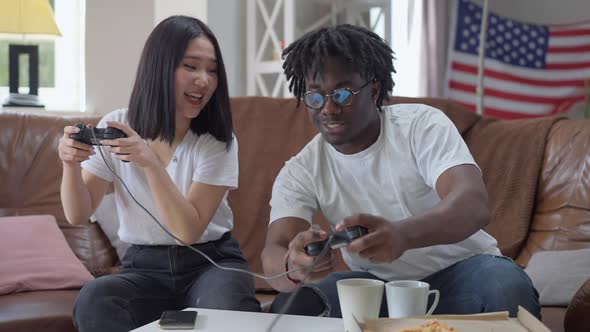 Front View of Joyful African American Boyfriend and Asian Girlfriend Having Fun Playing Video Game