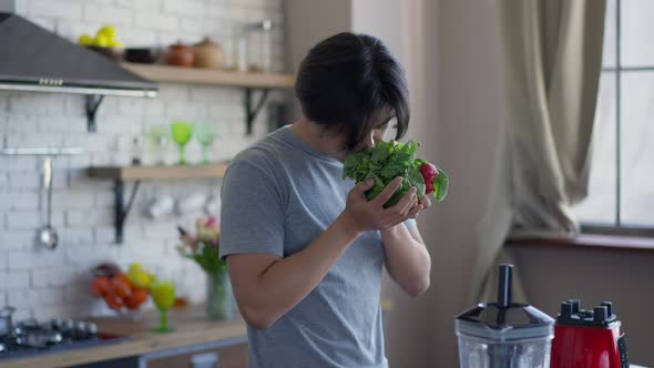 Camera Approaches to Young Asian Man Smelling Healthful Vitamin Organic Radish Standing in Kitchen