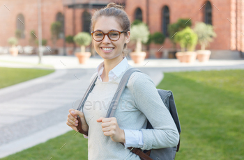 irl in university campus with big eyeglasses, pulling forward straps of backpack and looking at someone, feeing happy and eager to go together.