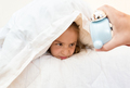 little girl covering head with pillow and looking at alarm clock - PhotoDune Item for Sale