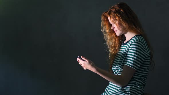 Beautiful young woman with red hair looking at smartphone