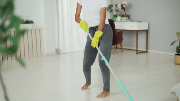 Funny African American Girl Is Enjoying Music in Headphones and Doing Housework Washing Floor at