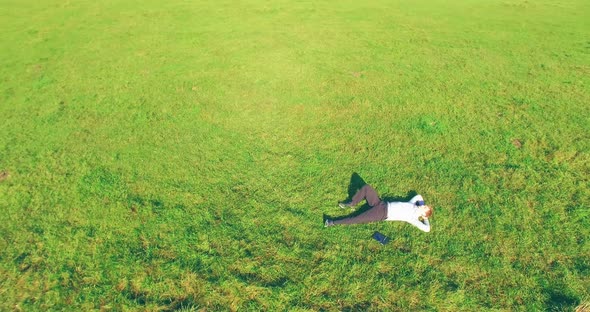 Low Orbital Flight Around Man on Green Grass with Notebook Pad at Yellow Rural Field.