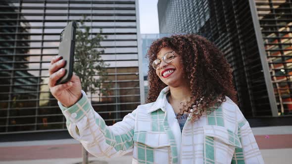 Curly African American Woman is Having a Call Using Her Smartphone Outdoors on Modern Buildings