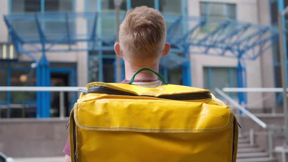 Young Man in Covid19 Face Mask with Yellow Food Delivery Bag Turning to Camera Standing in Front of