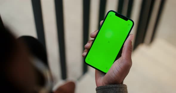 An African American Man Holds a Mobile Phone with a Green Screen in His Hand