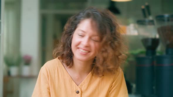 Smiling Curly Woman in Yellow Dress Dancing Happily While Sits in Coffee Shop