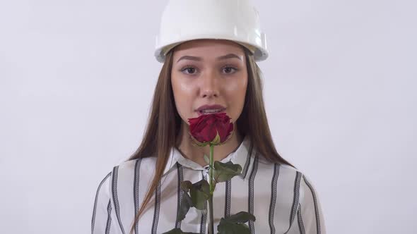 Young Beautiful Woman in Construction Hat Holding a Red Rose in Her Hands and Happy